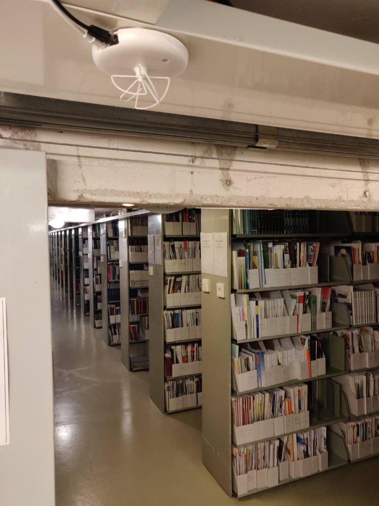 A long corridor of bookshelves. A ruuvi Gateway is placed on the roof with adhesive tape