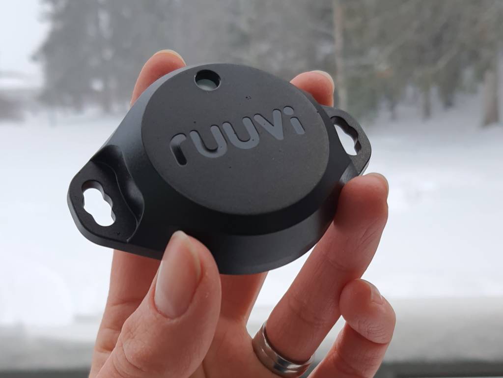 Black Ruuvitag Pro in hand in front of a snowy landscape.
