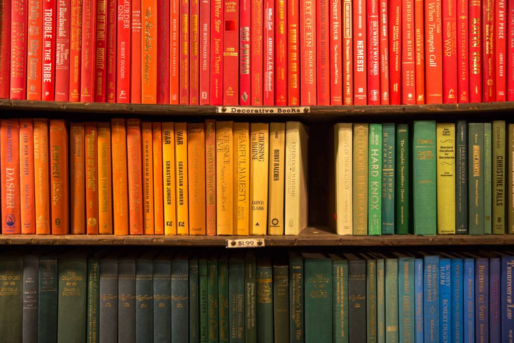 Different colored books on a bookshelf. Similiar sized books should be stored next to each other.
