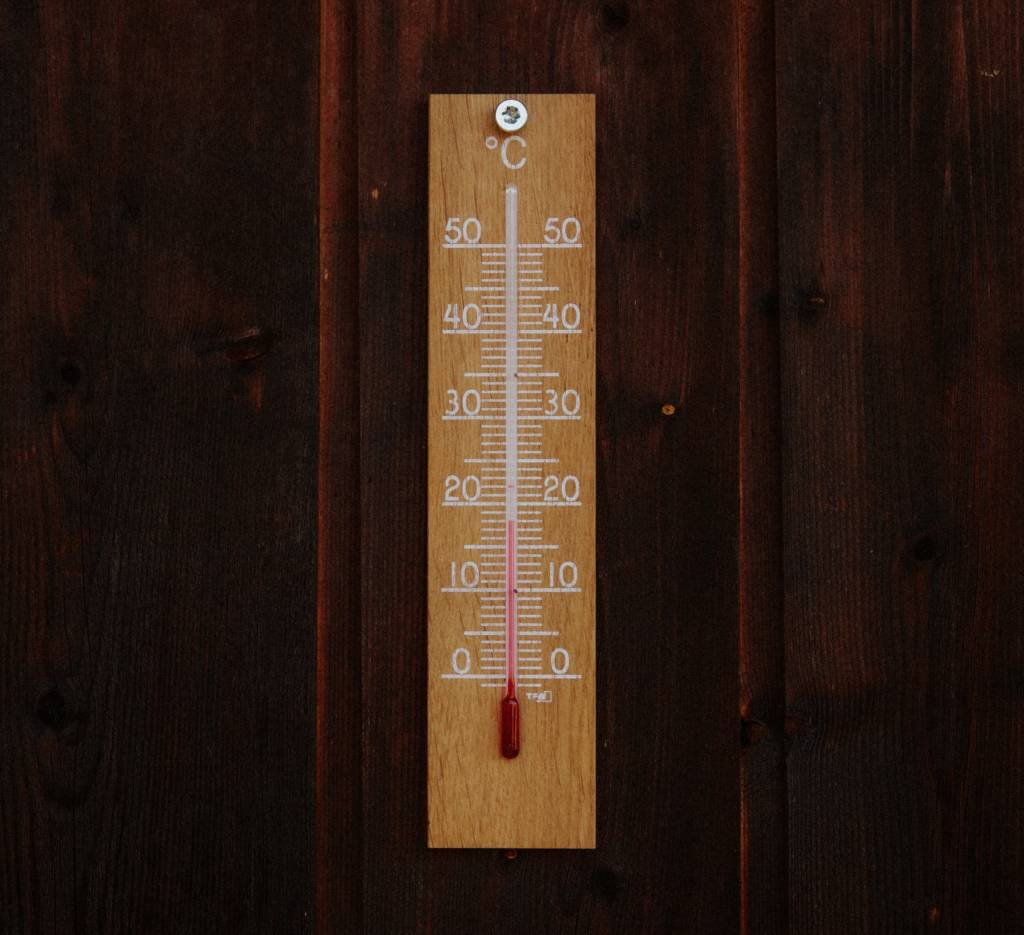 Older analog thermometer attached to a wall. 
